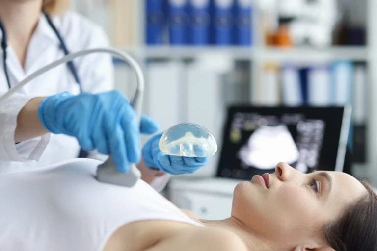 Ultraschall-Untersuchung zur Kontrolle der Brustimplantate Ärztin führt eine Ultraschall-Untersuchung nach einer Brustvergrößerung mit Implantaten an einer Patientin durch